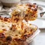 dumpling lasagna with golden crispy cheese and meat sauce pulled from baking dish with spatula