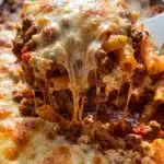 million dollar baked ziti with golden bubbly cheese crust being scooped from baking dish